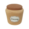 A round, beige-colored handcrafted Basket Honey Pot with a lid, labeled “honey” on a decorative white label with fancy black script. The texture of the Basket Honey Pot appears soft and tightly knit.