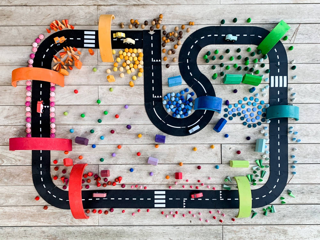 The WaytoPlay: Extra Long Flexible Road Set - King of the Road features black track pieces winding across a wooden floor, surrounded by colorful arches and blocks—ideal for imaginative play and inspiring problem-solving as toy cars race along.