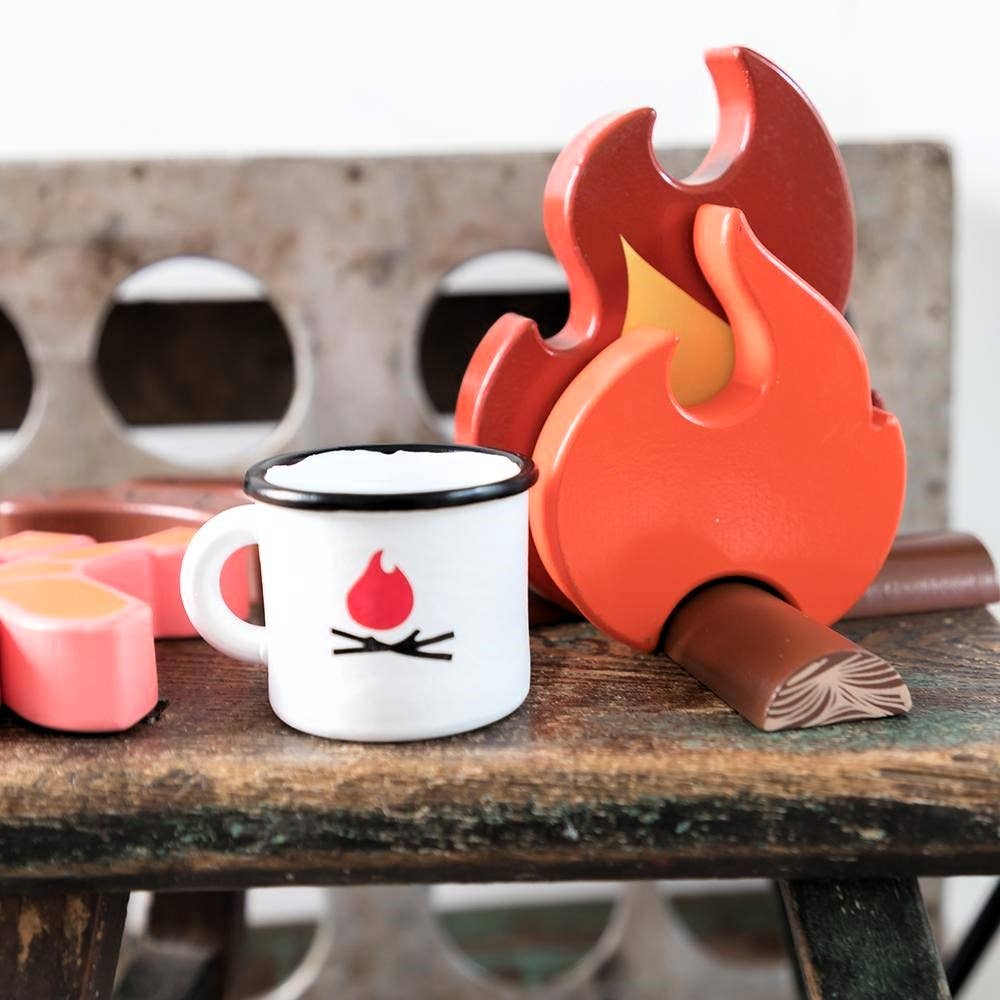 The Wooden Camp Fire Set includes wooden flames, a mug with a flame graphic, and toy marshmallows on a rustic surface—perfect for kids' indoor camping and pretend play.