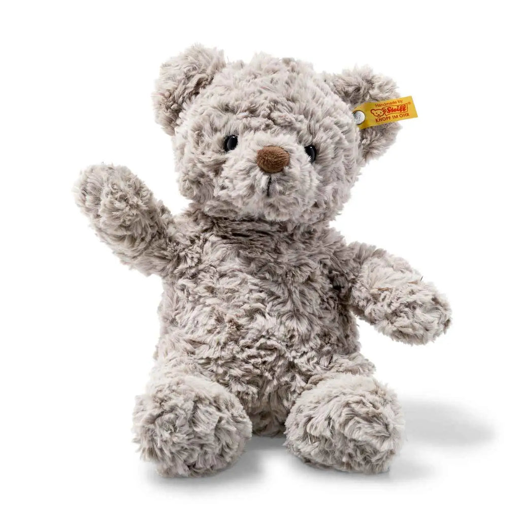 A soft, gray Steiff Honey Teddy Bear, 11 Inches with a textured fur finish, sitting upright and raising one paw, against a white background. This handmade bear features the iconic "Button in Ear" that distingu