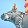 Close-up of a whimsical ceramic Hippo Cake Topper wearing a colorful striped party hat against a clear blue background.