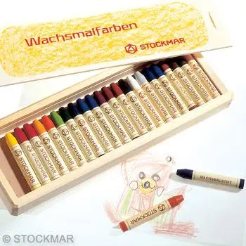 A box of Stockmar Wax Stick Crayons Wooden Box - 24 Assorted, open and displaying the crayons neatly arranged. Below the box, a child’s drawing of a bear and a couple of non-toxic