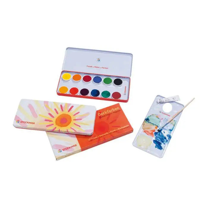A set of Stockmar Opaque Colors - 12 Colors watercolor paints with a brush, displaying an opened paint box and two painted cards featuring vibrant, artistic designs.