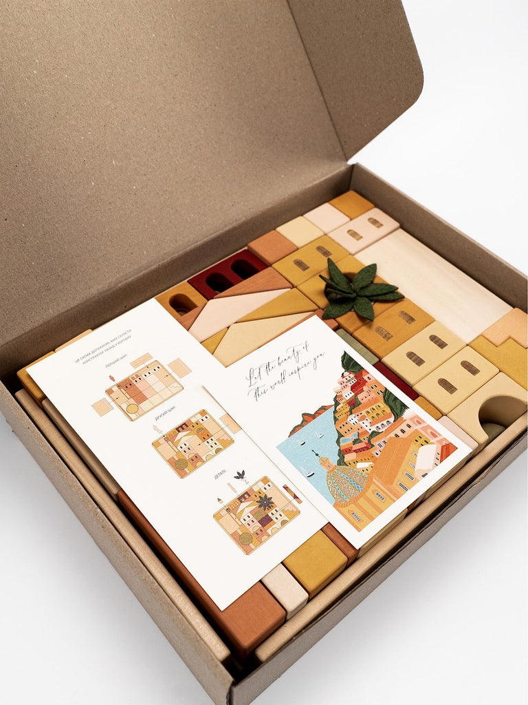 A beautifully arranged open gift box containing a collection of Sabo Concept Italian Ancient City Blocks, various wooden stamps, and a green leaf, all elegantly displayed against a crisp white background.
