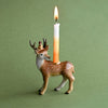 A whimsical Stag Cake Topper shaped as a hand-painted, spotted deer with a lit candle protruding from its back, set against a plain green background.