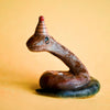 A close-up photograph of a small, intricately detailed hand-painted Snake Cake Topper figurine of a brown snake with red and blue accents, coiled on a soft yellow background.