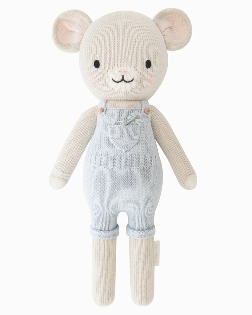 Cuddle + Kind Bailey The Mouse is a hand-knit doll with light beige fur, round ears, rosy cheeks, a smiling face, pale blue overalls, and filled with hypoallergenic polyfill.