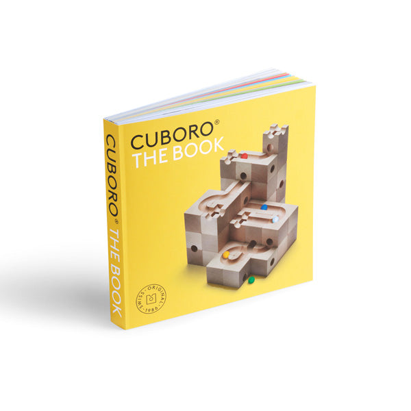 A hardcover book titled "Cuboro The Book" featuring a colorful image of a wooden block marble run on its cover. The book has a yellow spine and stands upright.