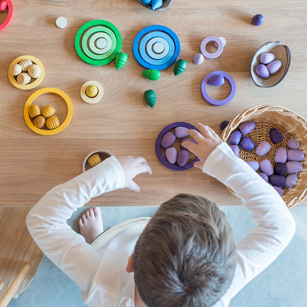 A child sitting at a wooden table playing with Grapat Nesting Rings, focusing intently on arranging them.