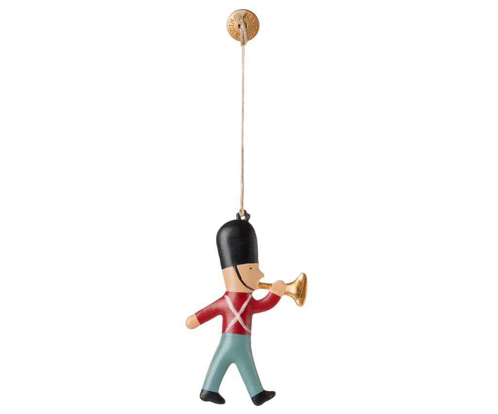 The Maileg Metal Ornament, Guard - Trumpet features a hand-painted toy soldier in a red jacket, blue pants, and black hat blowing a gold trumpet, perfect for your Christmas tree. Easily hangs by a string from a small round hook.