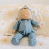A soft doll from the Olli Ella Dozy Dinkums - Bug Collection with a serene expression, dressed in a blue, star-patterned onesie and a matching hood, sits against a yellow cushion with large white d
