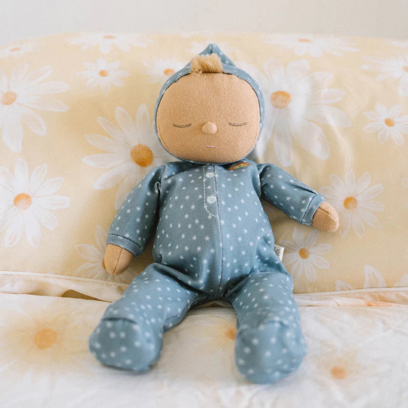 A soft doll from the Olli Ella Dozy Dinkums - Bug Collection with a serene expression, dressed in a blue, star-patterned onesie and a matching hood, sits against a yellow cushion with large white d