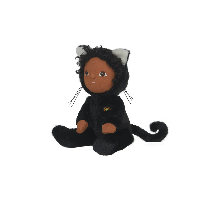 The Olli Ella Dinky Dinkum Doll - Carson Cat - Black, featuring brown skin and curly black hair in a velvet cat onesie with ears, tail, and a rainbow patch, sits upright against a white background—a perfect Halloween soft toy.