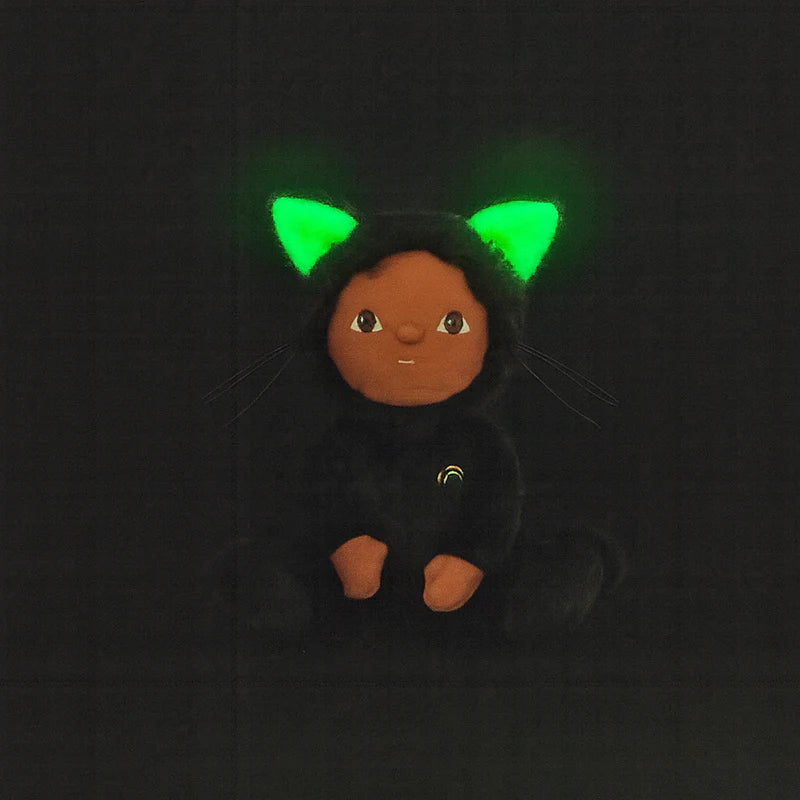 The Olli Ella Dinky Dinkum Doll - Carson Cat - Black is a plush toy with dark skin, a velvet onesie, glowing green cat ears, and stitched paws, shown against a black background with a neutral expression.