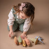 A young child is playing with a Handmade Wooden Triceratops Dinosaur, on a beige background. She is focused on arranging this handcrafted toy.