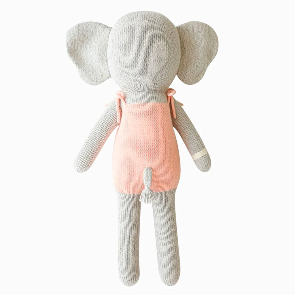 Cuddle + Kind Eloise the Elephant is a hand-knit gray elephant plush with large ears, dressed in a sleeveless pink outfit, displayed from the back on a white background.