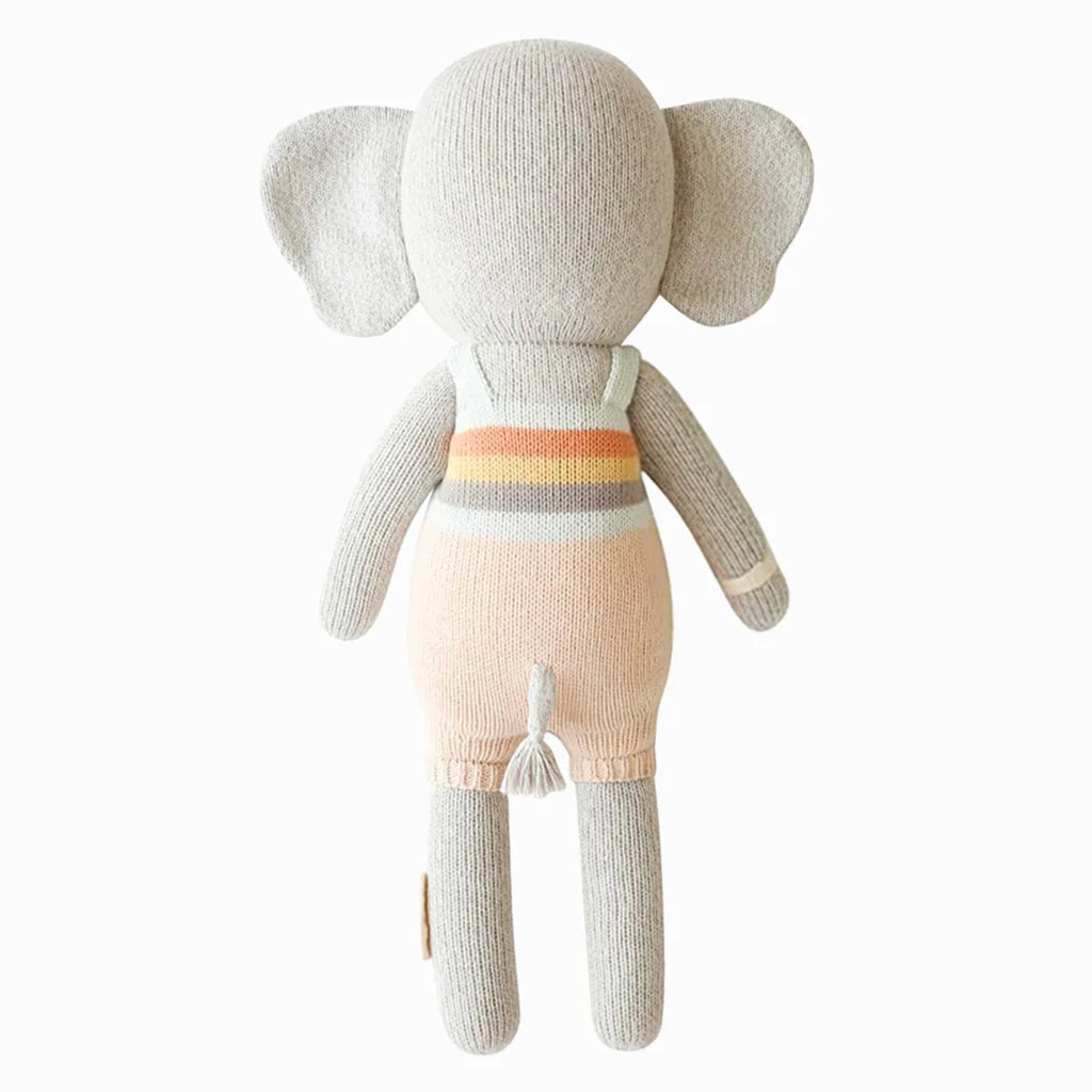 Cuddle + Kind Evan the Elephant is a hand-knit, stuffed elephant doll with large ears and a pastel striped outfit, shown from the back on a white background. Each purchase provides meals to children in need.