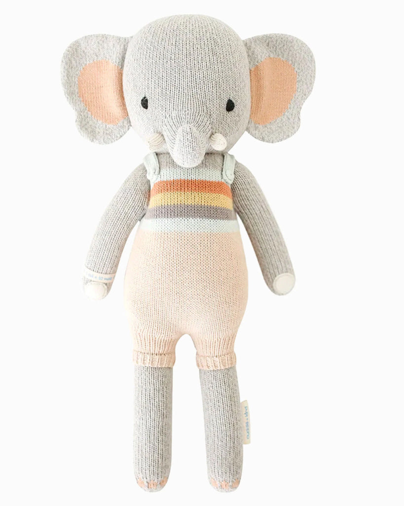Cuddle + Kind Evan the Elephant is a hand-knit stuffed doll with gray ears, trunk, limbs, pastel-striped outfit, white tusks, and blush inner ears. Each purchase helps provide meals to children in need.