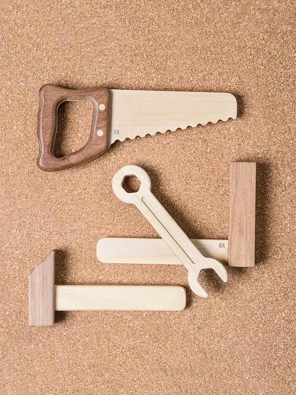 Sentence with Product Name: Heirloom quality Wooden Tool Set including a saw, wrench, hammer, and two blocks, arranged on a sandy-textured beige background.