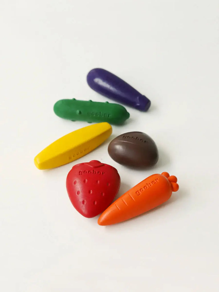 Six colorful Farm Crayons designed as a purple eggplant, green cucumber, yellow banana, brown potato, red strawberry, and orange carrot arranged on a white background to promote motor skills development.