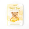 A children's book titled "Slumberkins Honey Bear Kin + Lesson Book On Gratitude" featuring an illustration of a smiling bear surrounded by flowers on a white background, designed to cultivate gratitude.