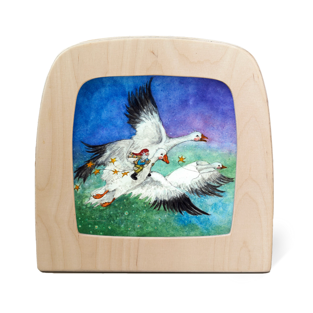 A child's illustration on a wooden frame, crafted with food-safe materials, shows two flying geese carrying a person in colorful garments. Stars trail behind, creating Magic Silhouettes against a shifting blue-to-green background. Product: Silhouette Only - George and the Snow Geese.