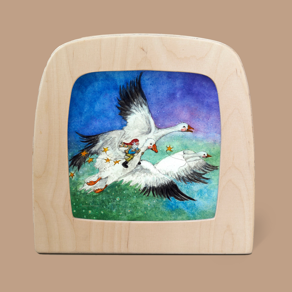 The artwork "Silhouette Only - George and the Snow Geese" depicts a small person riding a large white goose, flanked by two other geese as magical silhouettes against a blue-to-green gradient, all set in a wooden frame with a rounded top.