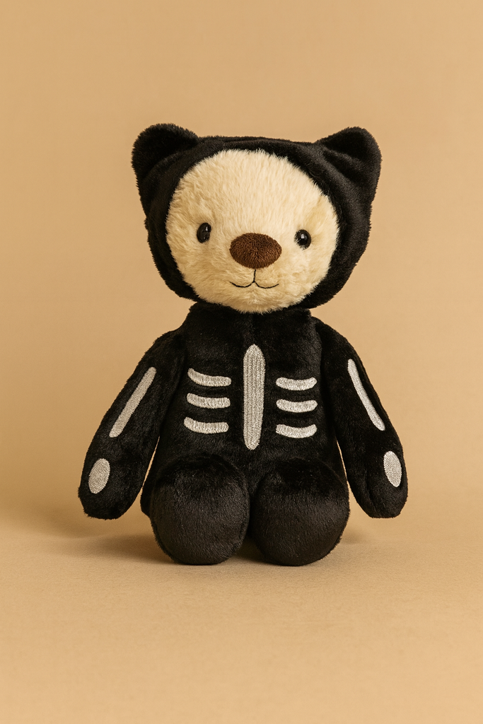 The Steiff Mr. Bones Teddy Bear from the Halloween plush collection, dressed in a black skeleton costume with a hood and white bone designs, sits against a beige background.