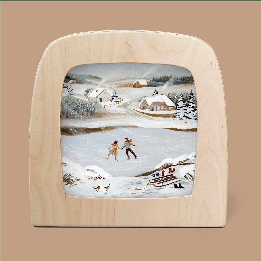 Product Name: Silhouette Only - Rosy Cheeks Silhouette for Toverlux Lamp (ships in approximately one week)
Description: An enchanting Rosy Cheeks Silhouette of a winter scene, framed in wood and crafted by Robin Pieterse. It features two magical silhouettes of people ice skating gracefully on a frozen pond, surrounded by snowy hills and quaint houses. A sled and pair of skates rest nearby, enhancing the idyllic landscape perfect for your Toverlux Lamp.