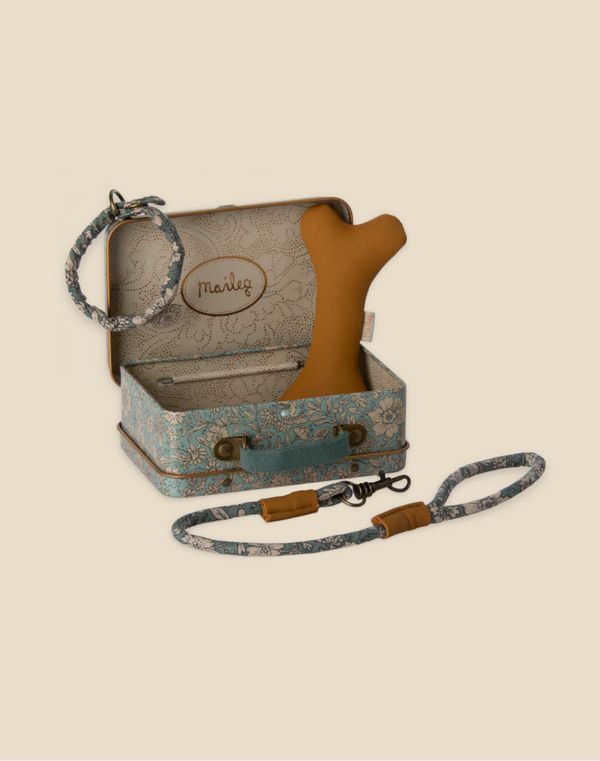 A decorative vintage-style suitcase with intricate floral patterns, containing a tan bone-shaped toy and a soft plush dog. Accompanying the suitcase are a floral-patterned collar and matching leash set, both with adjustable leather components. The suitcase has a label reading "Maileg Puppy Accessories - Blue.