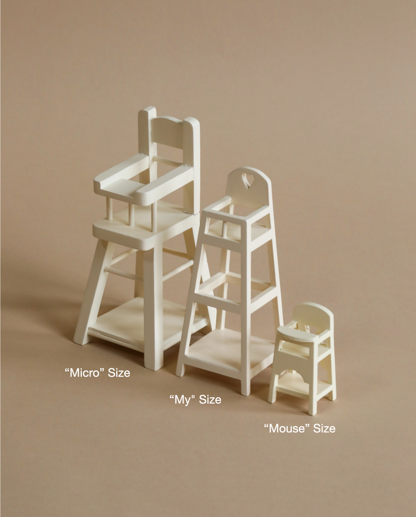 Three varying sizes of white wooden chairs displayed against a beige background, labeled as "Micro" size, "My" size, and "Maileg Mouse Size High Chair" size from largest to smallest.