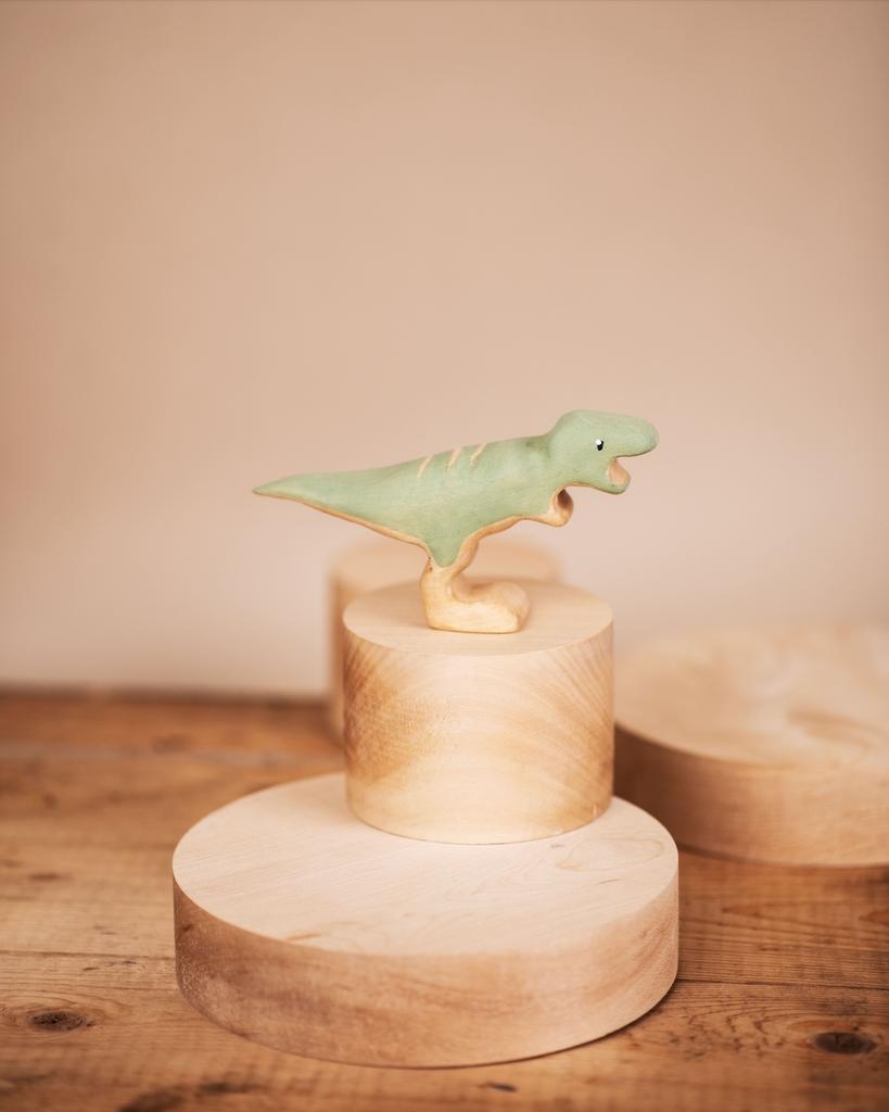 A Handmade Wooden T-rex Dinosaur perched atop cylindrical wooden blocks arranged in a tiered fashion, displayed against a warm beige background.