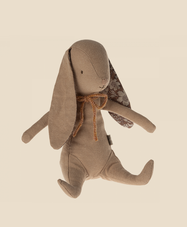 A soft bunny made of recycled polyester, this Maileg Bunny - Powder features long floppy ears detailed with a floral pattern on the inner side. With a stitched nose and eyes and a simple brown string bow around its neck, it also has magnets in its hands. The background is a light cream color.