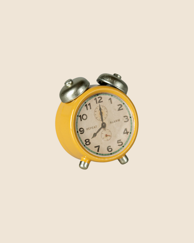 A Maileg Cozy Christmas Living Room Set features a small, mouse-size yellow vintage alarm clock with twin bells on top, showing 12:00, set against a plain beige background.