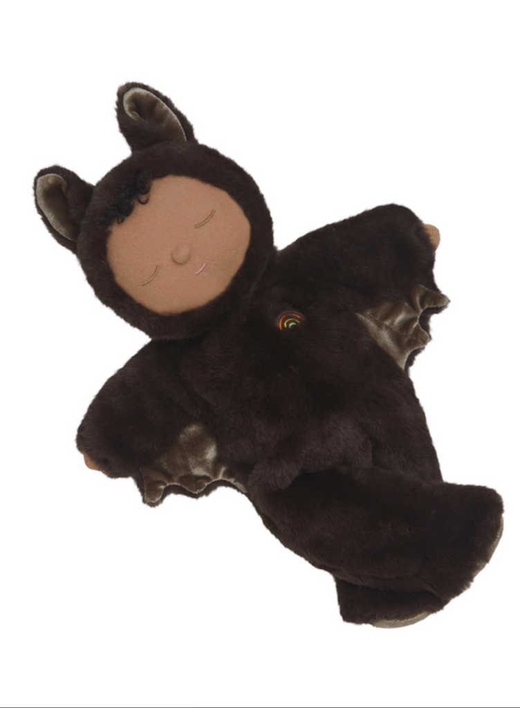 Olli Ella Cozy Dinkum - Bat Ozzie - Dark Umber is a cuddly bedtime toy with a tan face, black curly hair, closed eyes, and a soft dark brown bat costume featuring ears, wings, and a small rainbow embroidered on its chest.