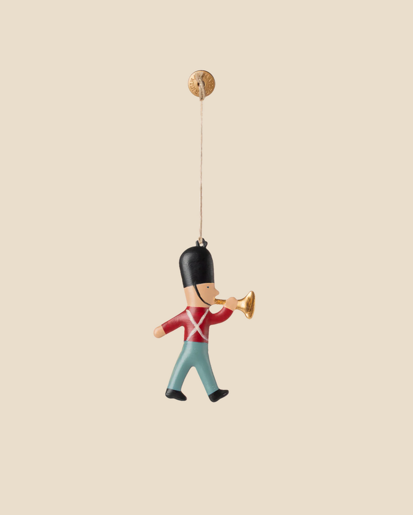 The Maileg Metal Ornament, Guard - Trumpet features a marching toy soldier in a red coat and blue pants playing a golden trumpet—a charming holiday decoration for your Christmas tree.