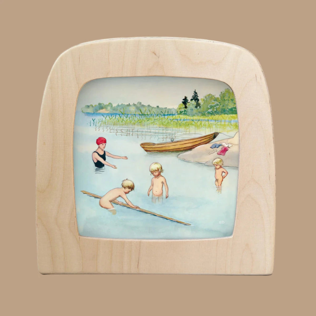 Illustration of three children and an adult enjoying a day at the lake, waist-deep in water with one holding a stick. Bathed in Silhouettes, this scene captures nature and togetherness within its wooden frame. Perfect for the Toverlux Lamp, "Silhouette Only - Around The Year (June).