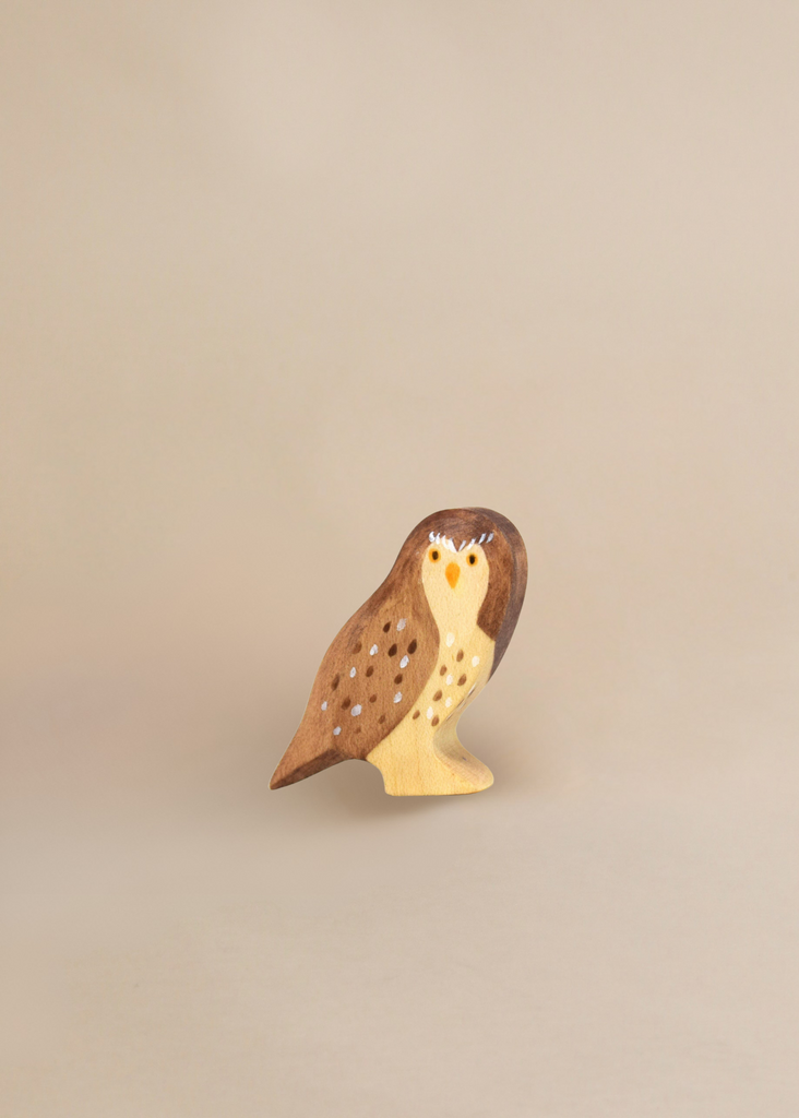 The Handmade Wooden Little Owl, crafted from sustainable hardwood and finished with natural plant-based stains in brown and cream, is shown against a plain beige background.