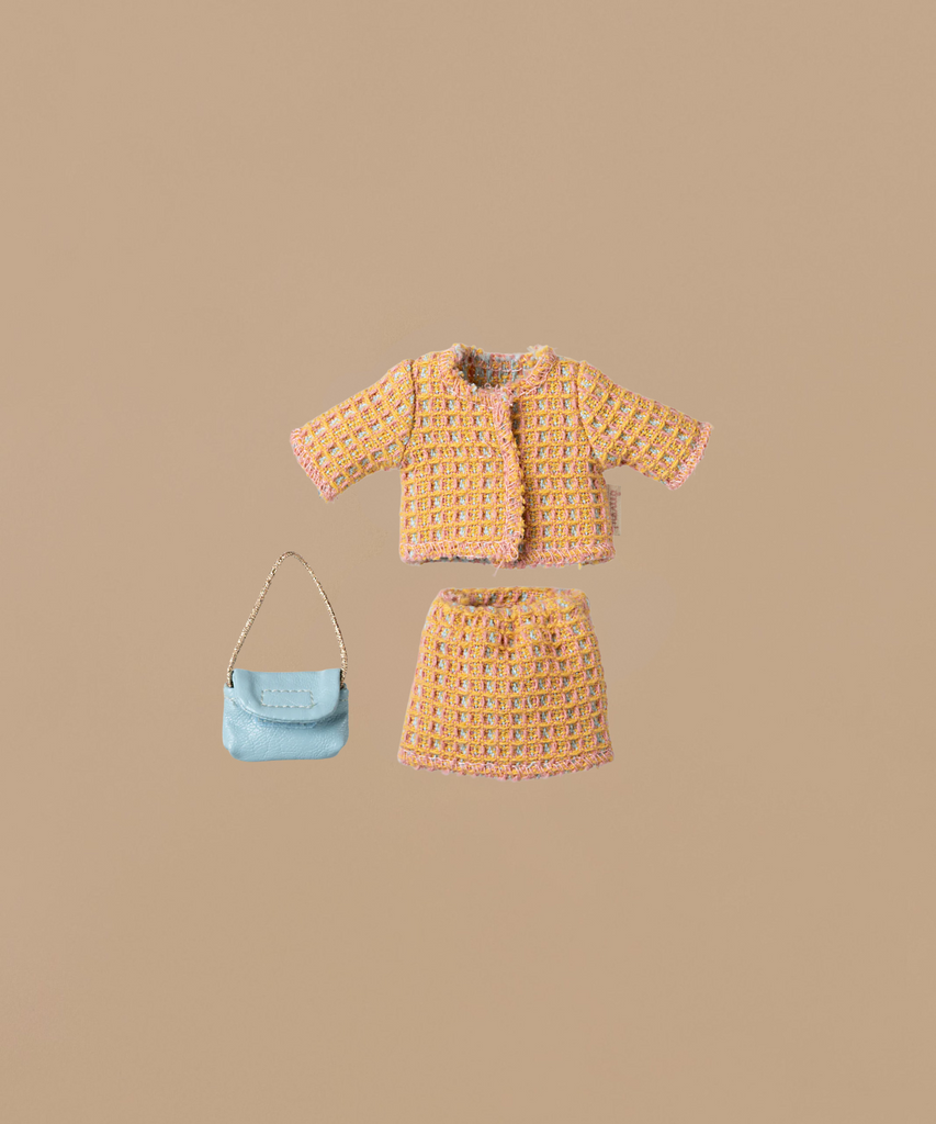 The Maileg Suit For Mum Mouse, featuring a doll-sized yellow and pink tweed jacket and skirt set, is beautifully displayed. Complementing the outfit is a small light blue handbag with a chain strap, all shown against a neutral beige backdrop.