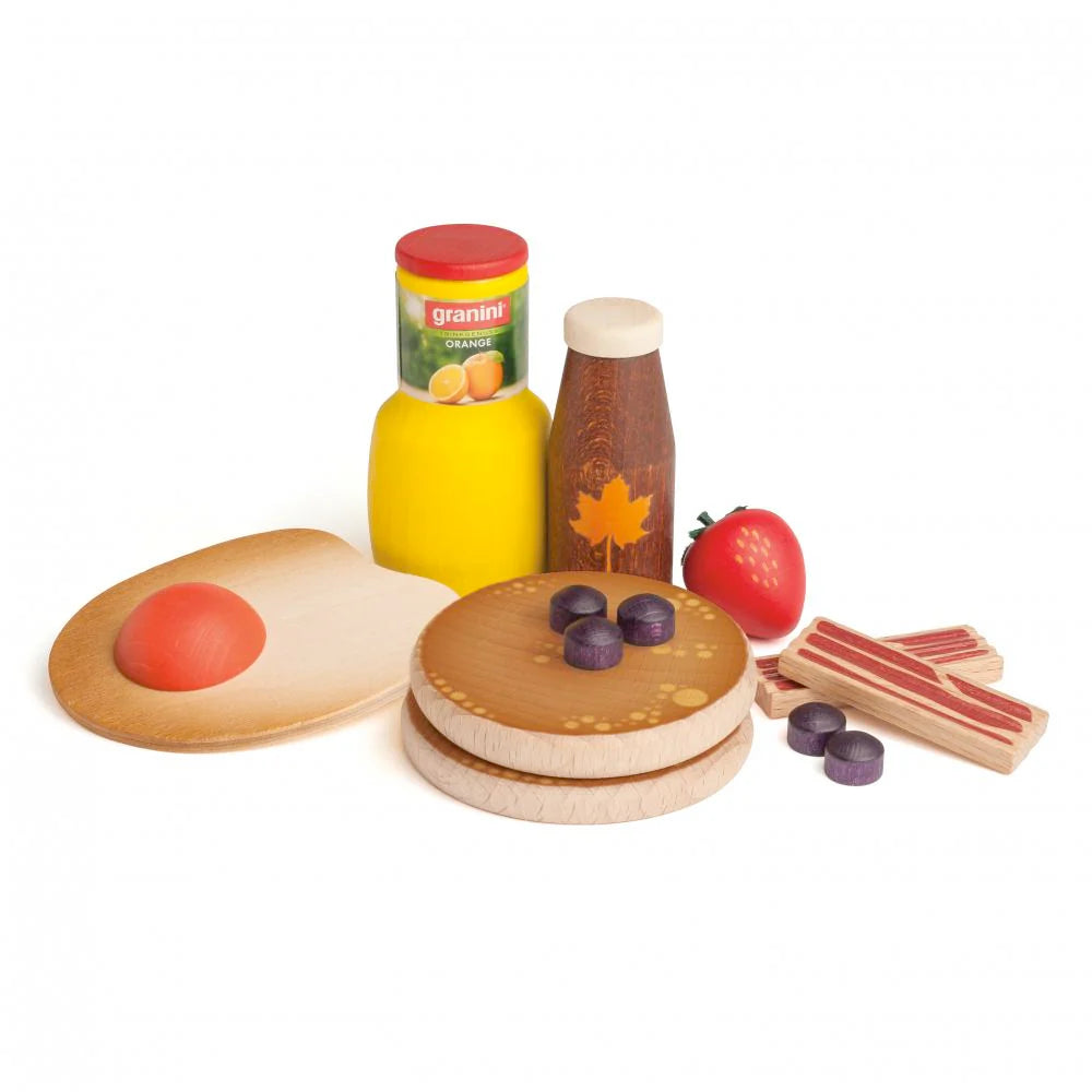 The Erzi American Breakfast Set features wooden toy foods including orange juice, maple syrup, a strawberry, bacon strips, pancakes with blueberries, and a cutting board topped with a fried egg.