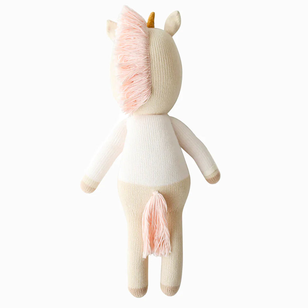 Cuddle + Kind Zara the Unicorn is a handmade knitted stuffed unicorn toy featuring a cream body, light pink mane and tail, and a small golden horn, shown from the back on a plain white background.