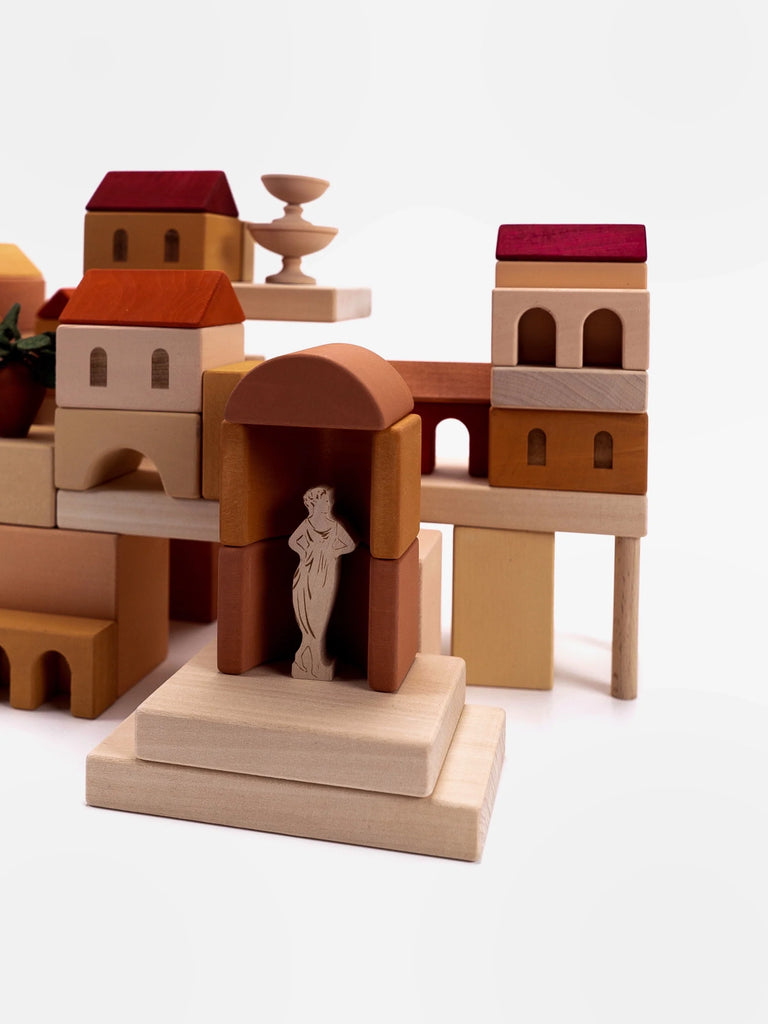 A model of a Mediterranean village made from Sabo Concept Italian Courtyard Blocks, featuring small houses, detailed arches, and a miniature statue at the center. The color palette includes earth tones with some red.