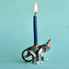 A whimsical Monkey Cake Topper shaped like a monkey wearing a red party hat, with a lit beeswax birthday candle on its back against a light blue background.