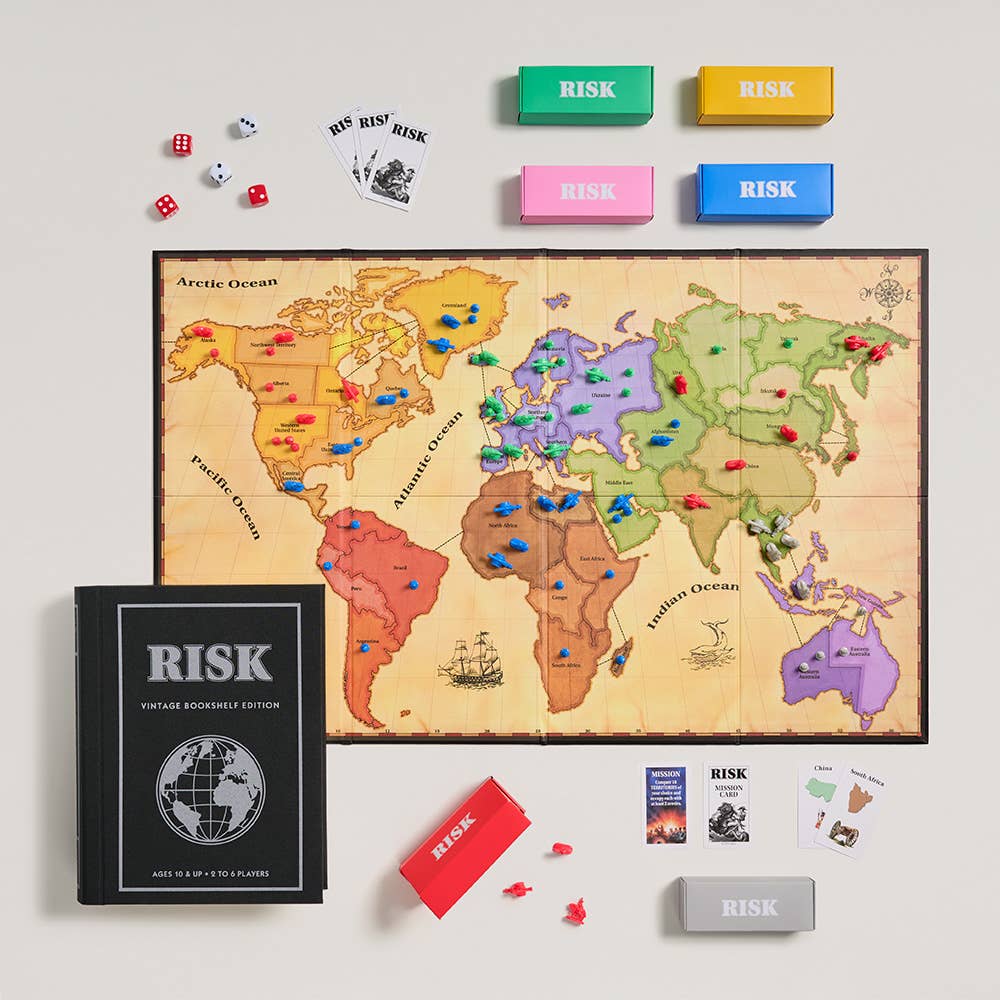 A Risk board game setup is displayed, featuring the Board Game: Risk Vintage Bookshelf Edition with a 1996-inspired board, colored army pieces, RISK cards, dice, five storage boxes, and the included game box and instructions.