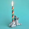 A colorful twisted candle is lit and mounted on the back of a hand-painted porcelain Dalmatian Cake Topper against a light turquoise background.