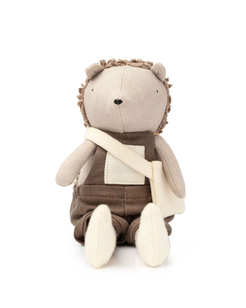 Harold The Hedgehog, from the Hedgehog Family, sports brown overalls and a crossbody bag. With a textured back resembling spines, he sits against a white background, poised for secret garden adventures with his cozy companions.