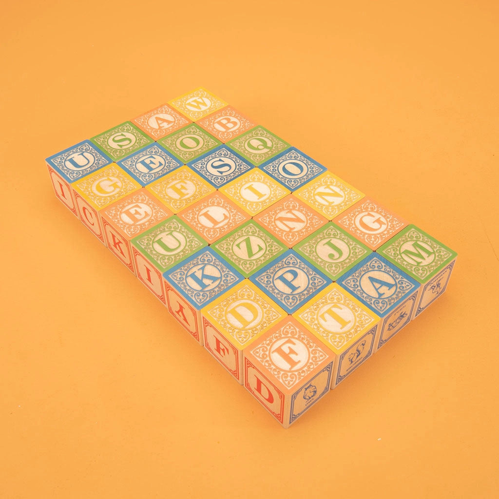 A set of Uncle Goose Classic ABC Blocks arranged on a light orange background, featuring a variety of letters in different colors and intricate borders.