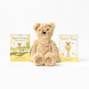 A plush teddy bear, Slumberkins Honey Bear, sits between two children's books titled "Slumberkins Honey Bear's Gifts of Nature" and "Slumberkins Honey Bear," against a white background.