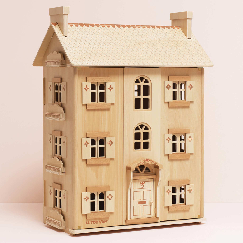 The Grand Natural Wood Doll House is crafted from sustainable wood, with two chimneys, four windows per floor, decorative shutters, a detailed front door, etched details, and "Le Toy Van" branding—perfect for imaginative play.