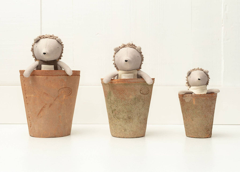 Three plush Harold The Hedgehog toys with gray bodies peek out of terracotta pots of varying sizes, ready for secret garden adventures against a white background. The smallest pot is on the right, and the largest is on the left.